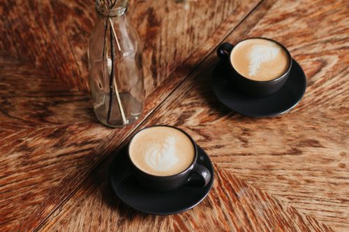 Free Two coffee cups with latte art on a wooden table beside a decorative vase, creating a cozy ambiance. Stock Photo
