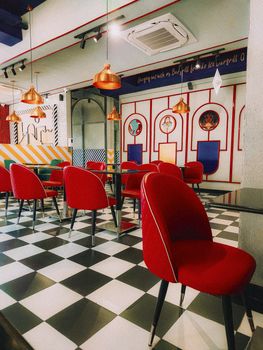A vibrant café interior featuring red chairs, checkerboard floor, and creative design elements.