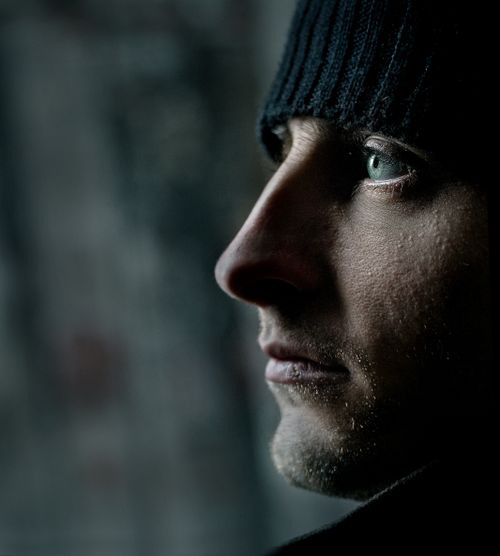 Free Side profile of a man wearing a knit hat, with dramatic lighting emphasizing his green eyes. Stock Photo
