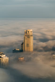一座高大的摩天大楼耸立在雾蒙蒙的城市中，四周环绕着厚厚的云层