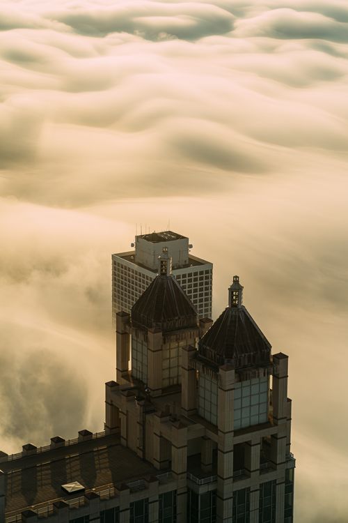 Free Captivating view of skyscraper towers peeking through low-lying clouds at sunrise. Stock Photo