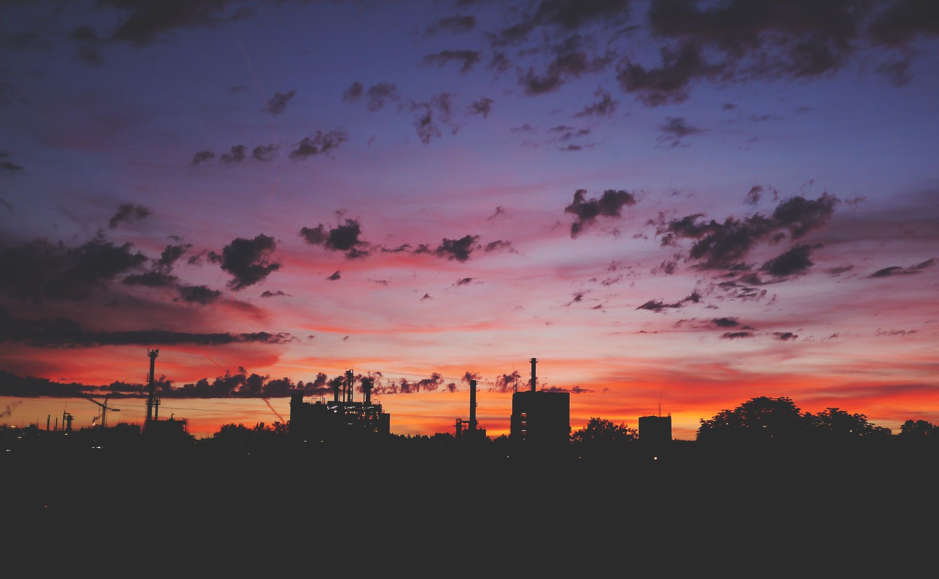 Silhouette of an industrial skyline against a vibrant sunset with colorful clouds.