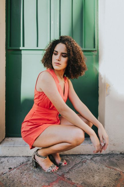 Glamorous woman with curly hair posing outdoors in a red dress, showcasing fashion and style.