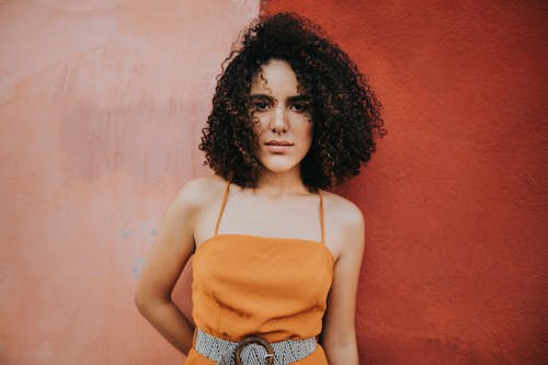 Woman wearing an orange top standing beside pink wall