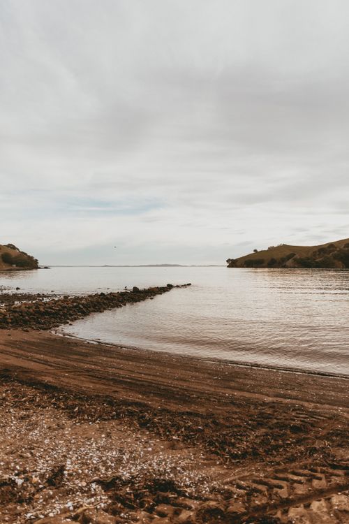 Free Tranquil beach scene in Kereta, Waikato, showcasing the calm sea and scenic hills under a cloudy sky. Stock Photo