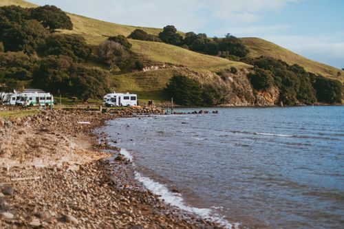 Free Tranquil campsite along the Coromandel coast with lush hills, trees, and sea views. Stock Photo