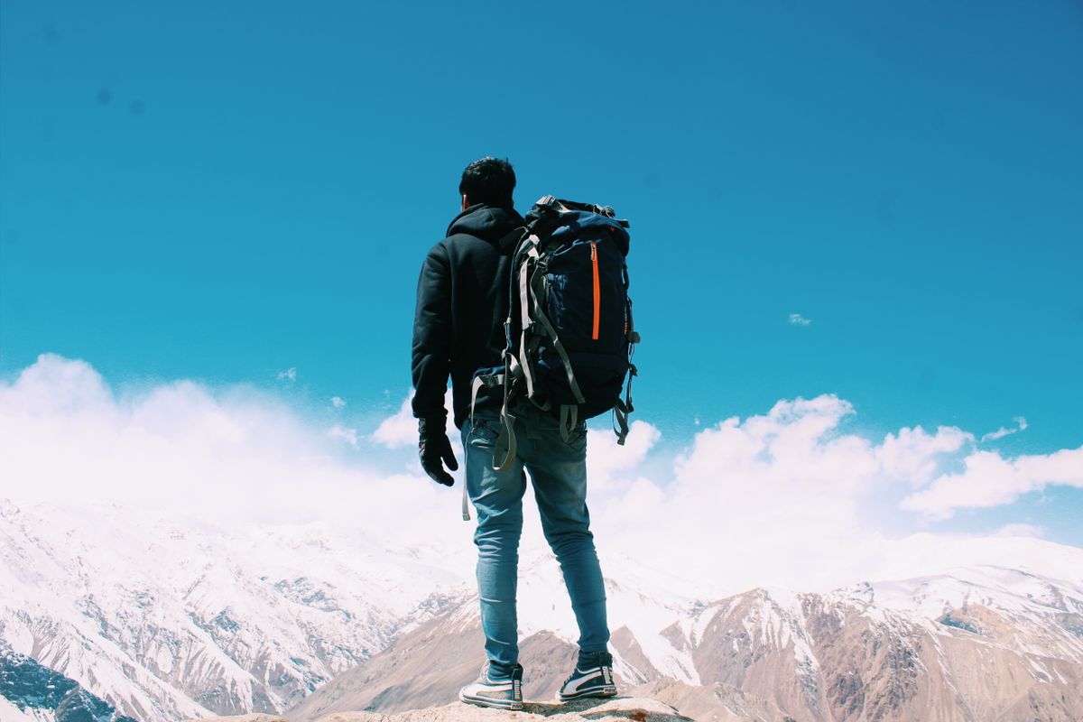 A lone hiker with a backpack surveys snow-capped mountains under a clear blue sky