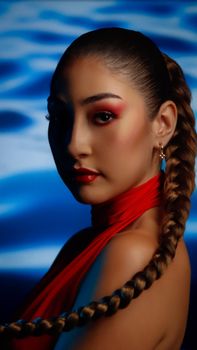 Portrait of a woman with bold makeup and braided hair against a blue background.