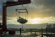 在港口充满活力的日落下，起重机吊起帆船，凸显了工业和海事主题