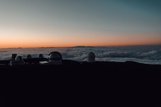 Silhouetted observatories atop Mauna Kea with a dramatic sunset over the clouds.
