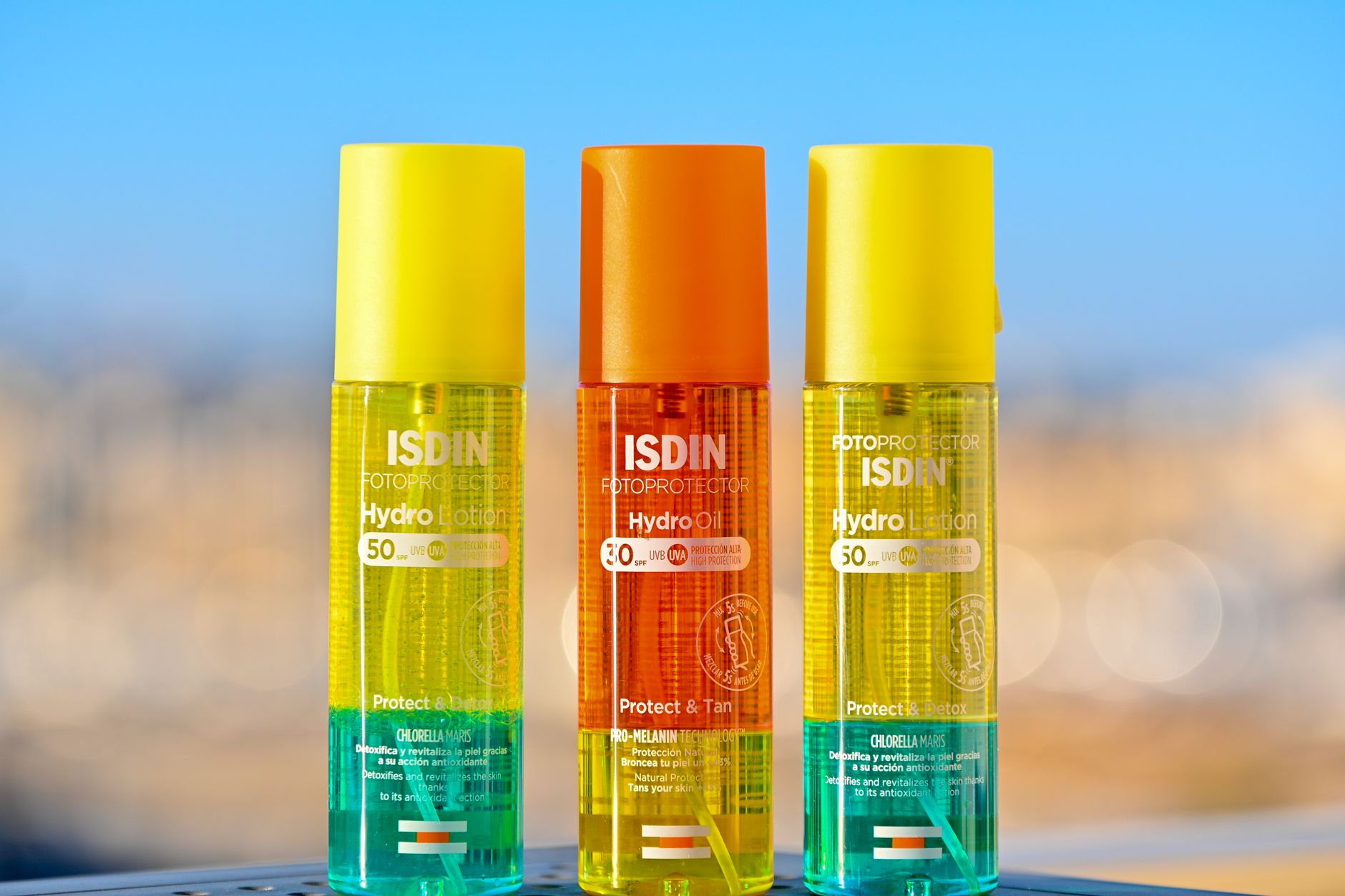 Three colorful ISDIN sun protection bottles against a blurred background, showcasing vibrant packaging.