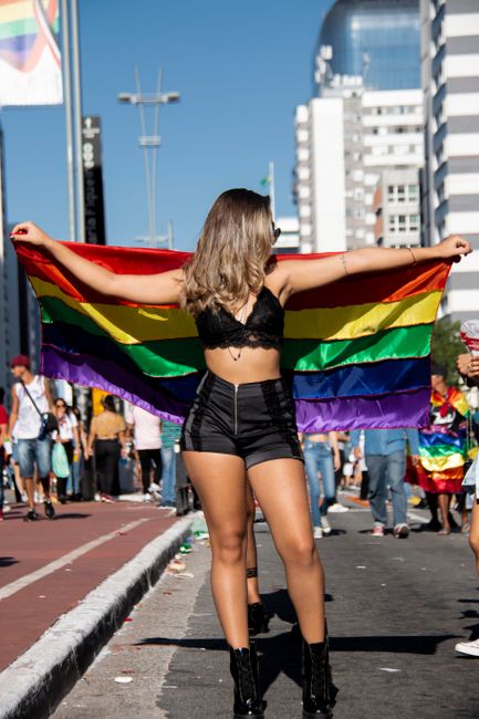 Woman holding rainbow flag during a lively outdoor gay pride parade.
