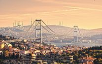 从空中俯瞰伊斯坦布尔博斯普鲁斯海峡大桥，背景是日落时分的城市天际线