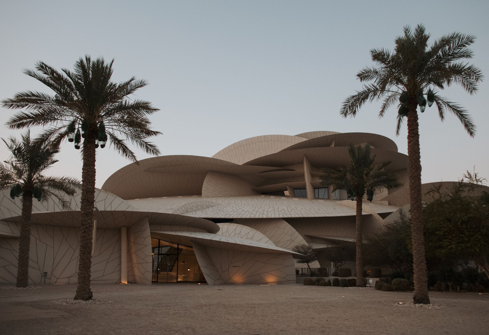 Stunning view of the National Museum of Qatar with palm trees at twilight, showcasing its unique architecture.