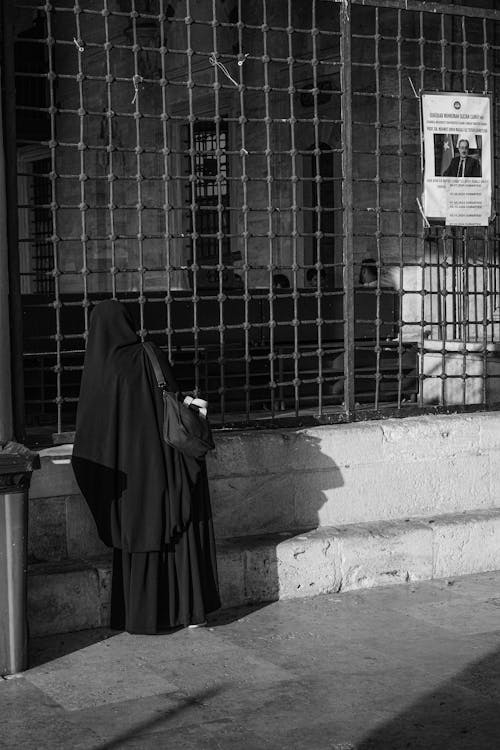 A woman in a black robe standing in front of a gate
