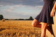 在阳光明媚的麦田里，一名穿着圆点连衣裙的妇女靠在干草捆上