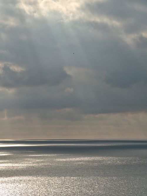 Free Peaceful ocean scene with sunlight streaming through clouds, creating a calming atmosphere. Stock Photo