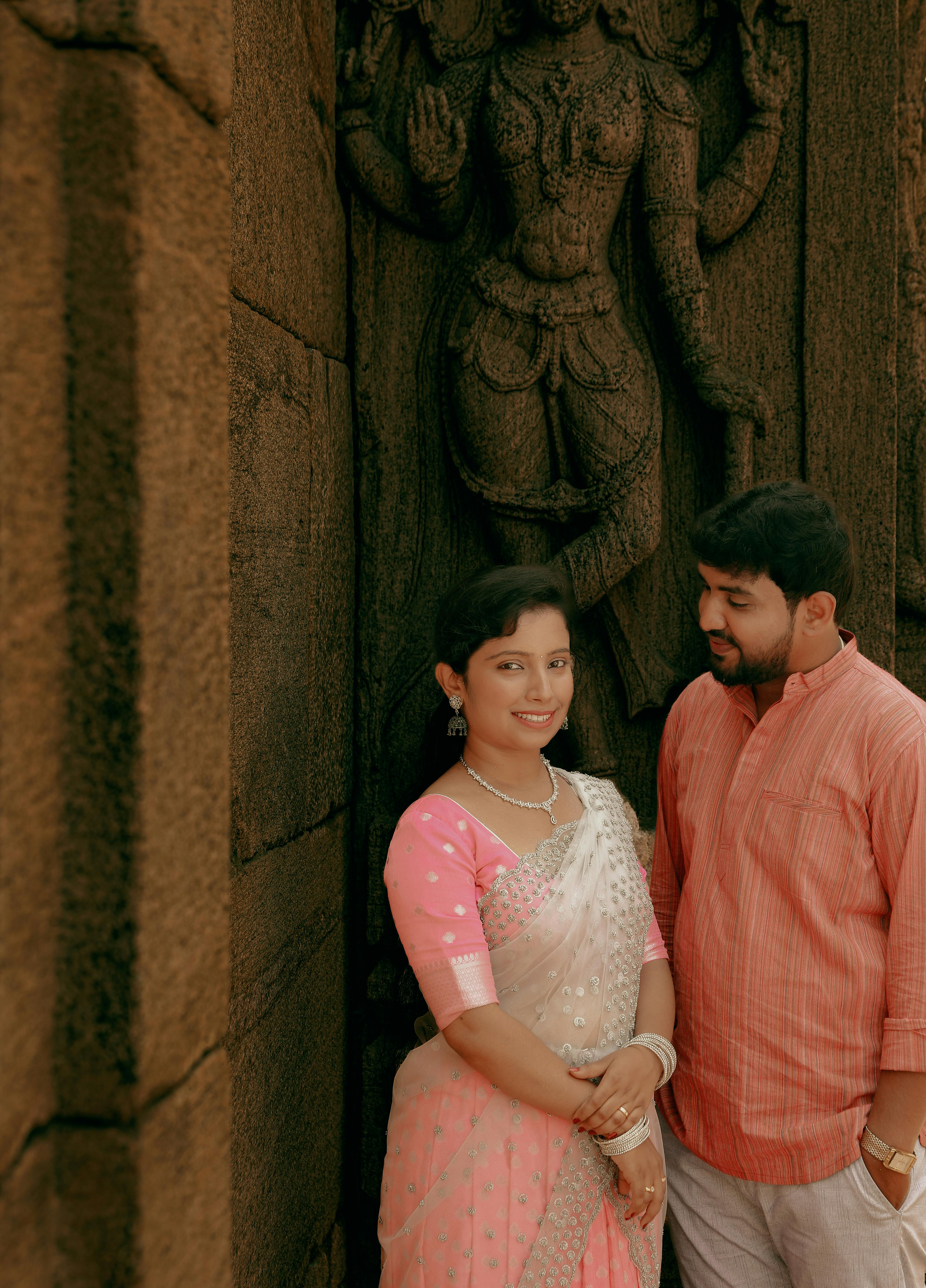 A couple posing against ancient stone carvings, showcasing traditional Indian clothing.