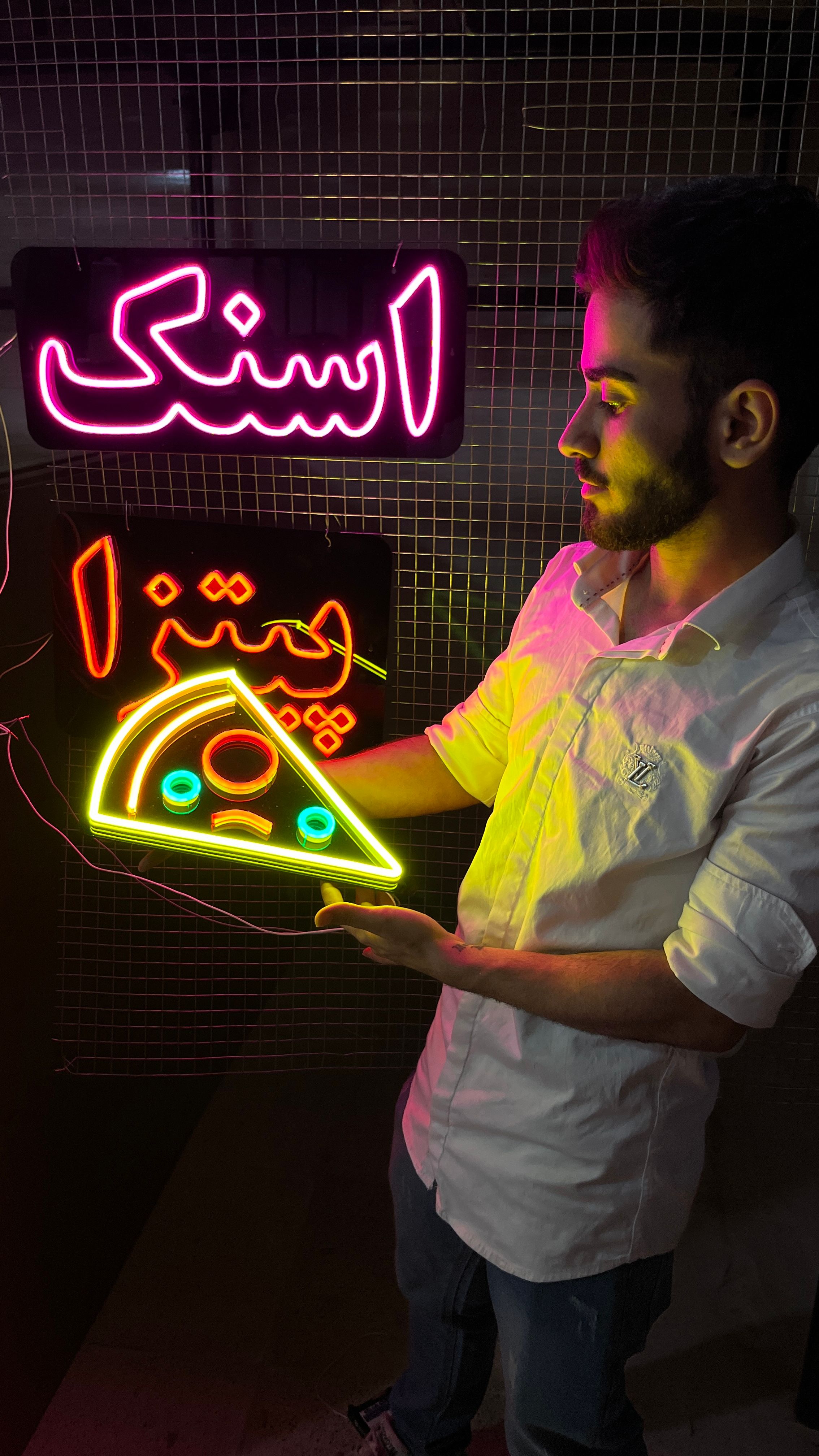 A man holding a neon pizza sign under colorful neon lights in Tehran, Iran.
