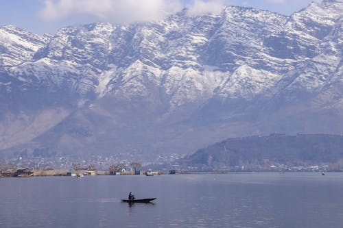 A man is in a small boat on the water with mountains in the background
