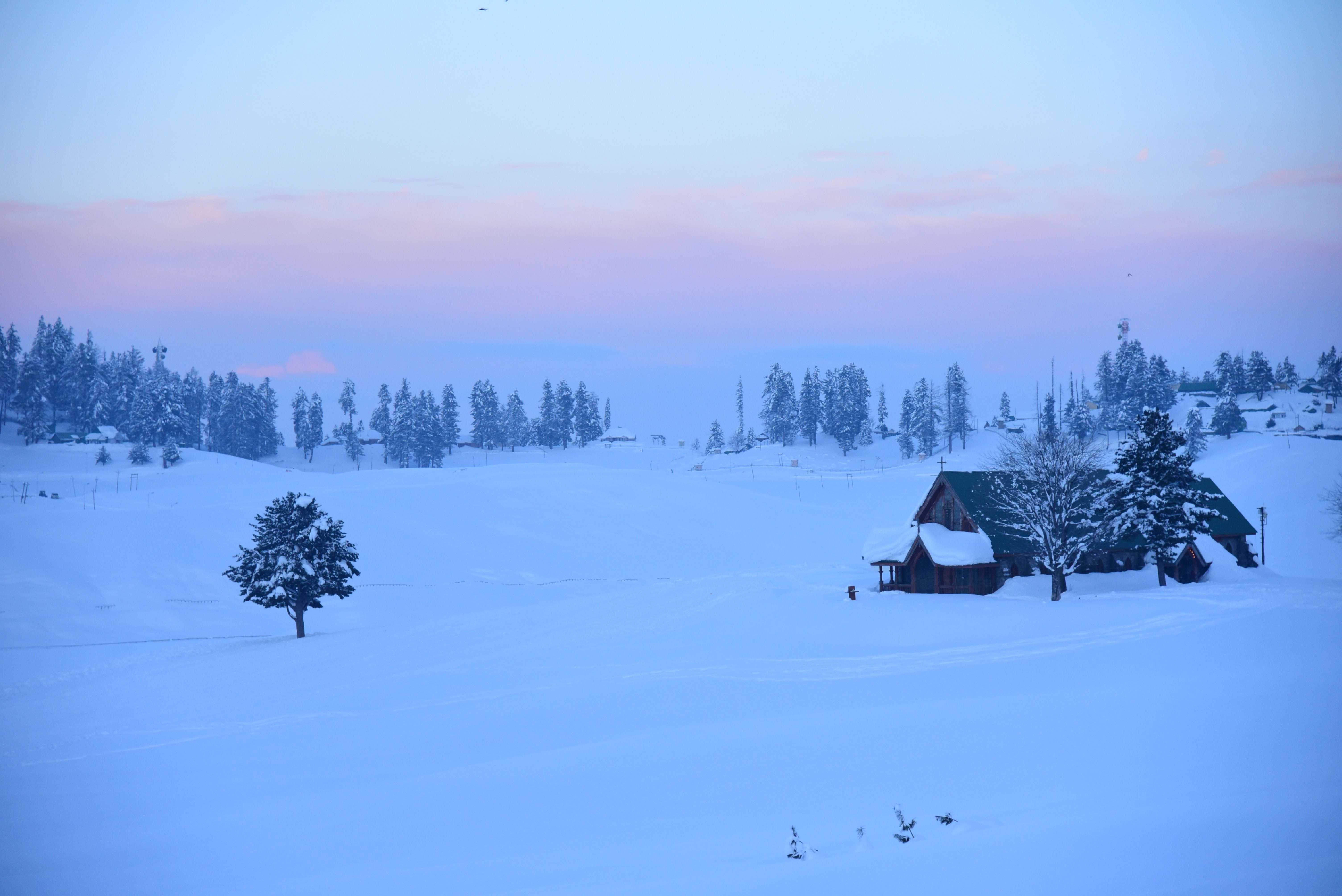 A tranquil winter scene in Gulmarg showcasing snow-covered landscapes and a quaint house during sunset.