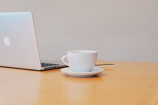 A clean and modern workspace featuring a laptop and a white coffee cup on a wooden desk.
