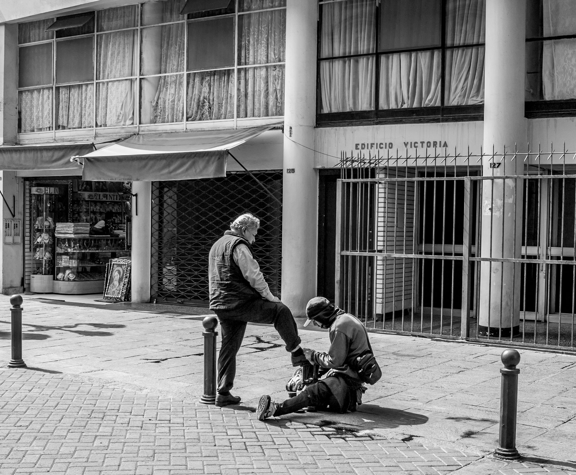 Black and white photo of a shoeshine on a busy street in Lima, Peru.