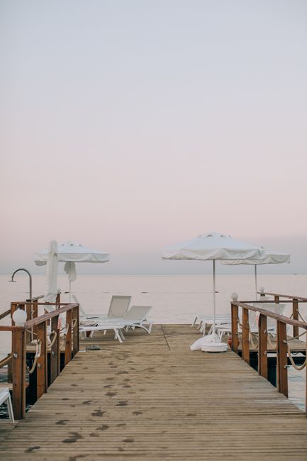 Peaceful view of a wooden jetty with umbrellas and sun loungers at sunset, perfect for relaxation.