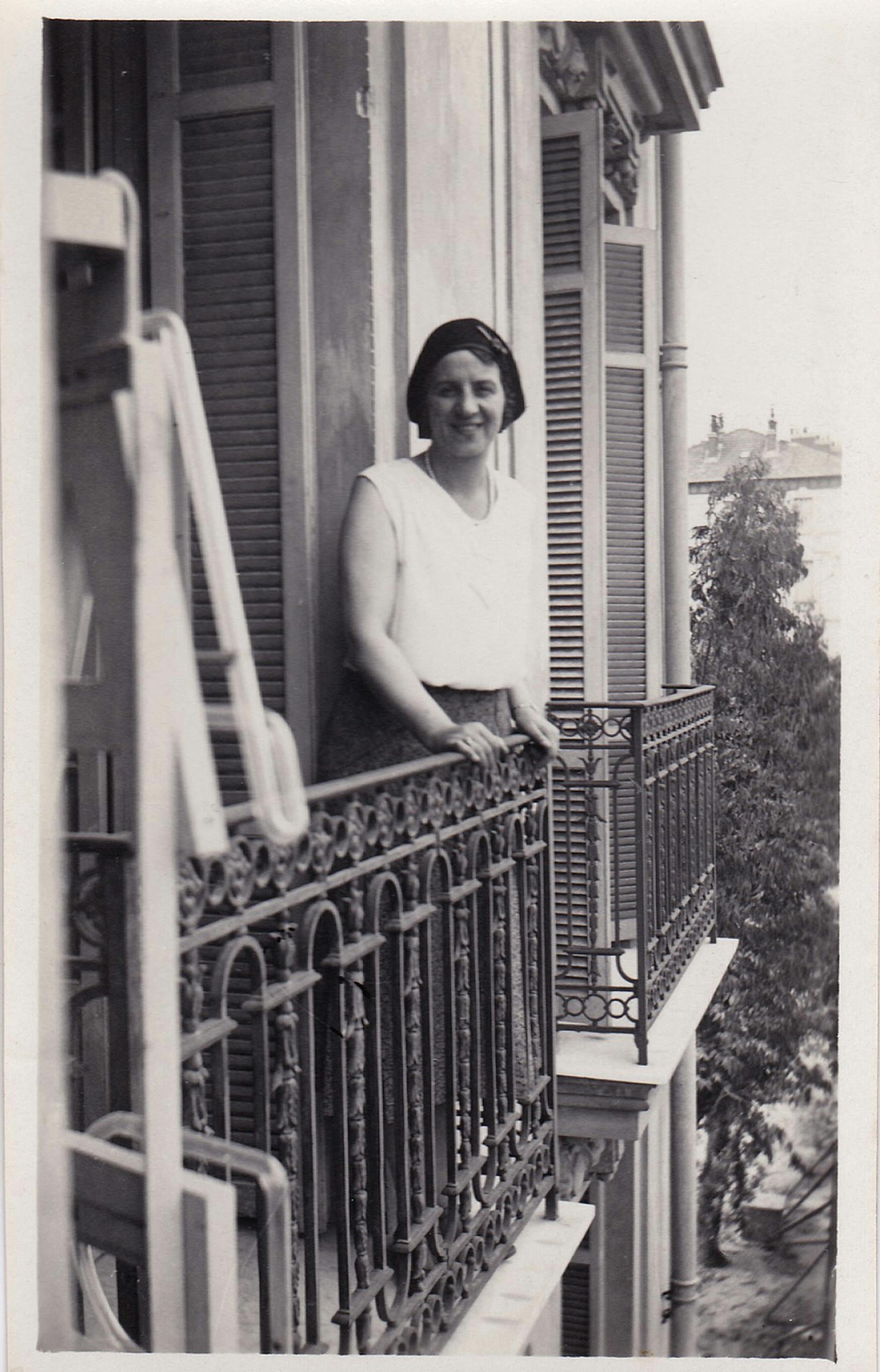 A nostalgic black and white photo of a woman smiling on a vintage balcony in a historic district.