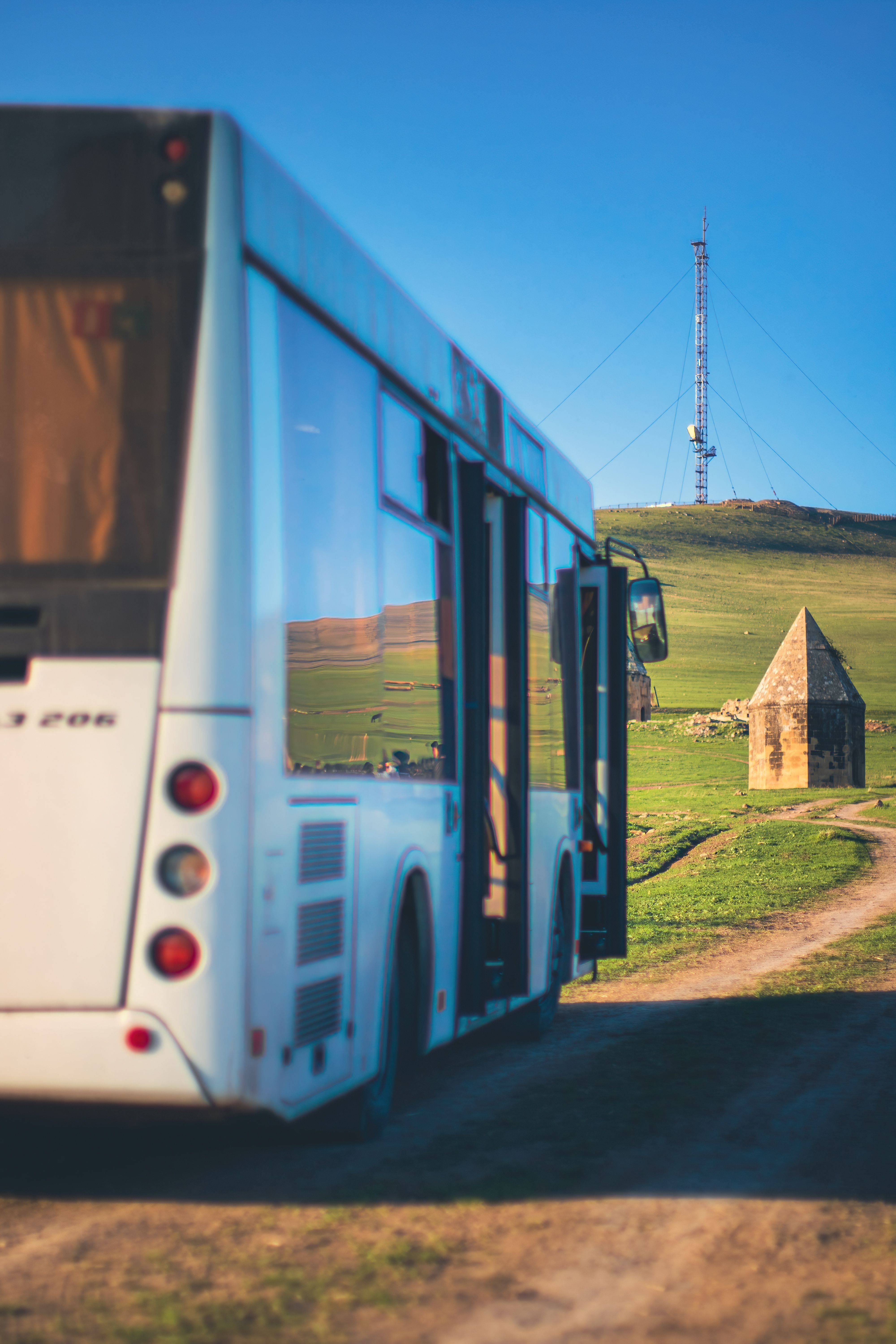 A white bus on a dirt road passing a rural landmark under clear blue skies.
