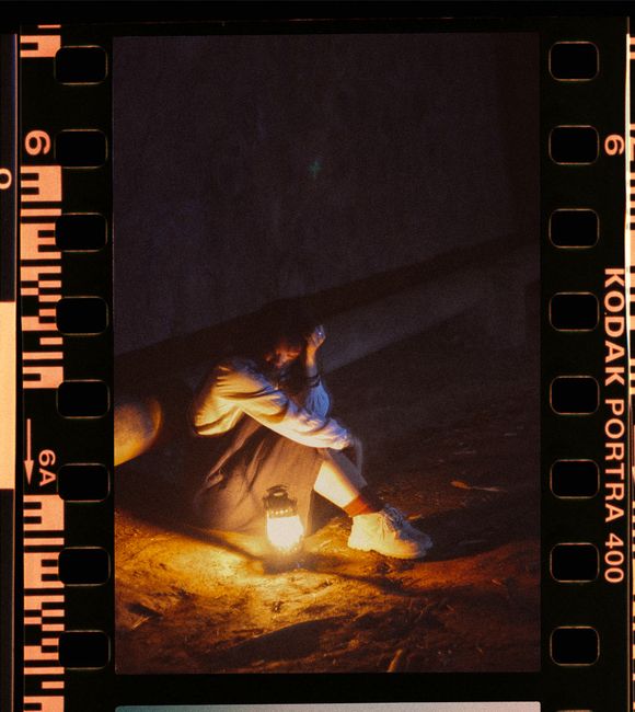 A woman sits alone with a lantern, casting a warm glow in the darkness.