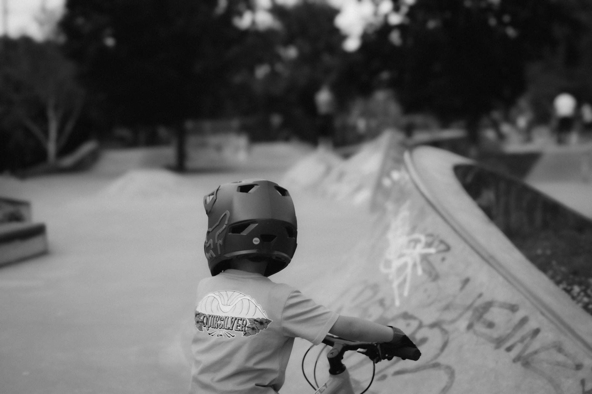 Young boy with helmet biking in an urban skate park, captured in black and white for a classic look.