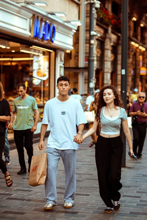 Free A young couple holding hands while walking on a busy city sidewalk. Urban lifestyle scene. Stock Photo