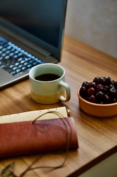 A warm workspace featuring coffee, laptop, and a bowl of cherries.