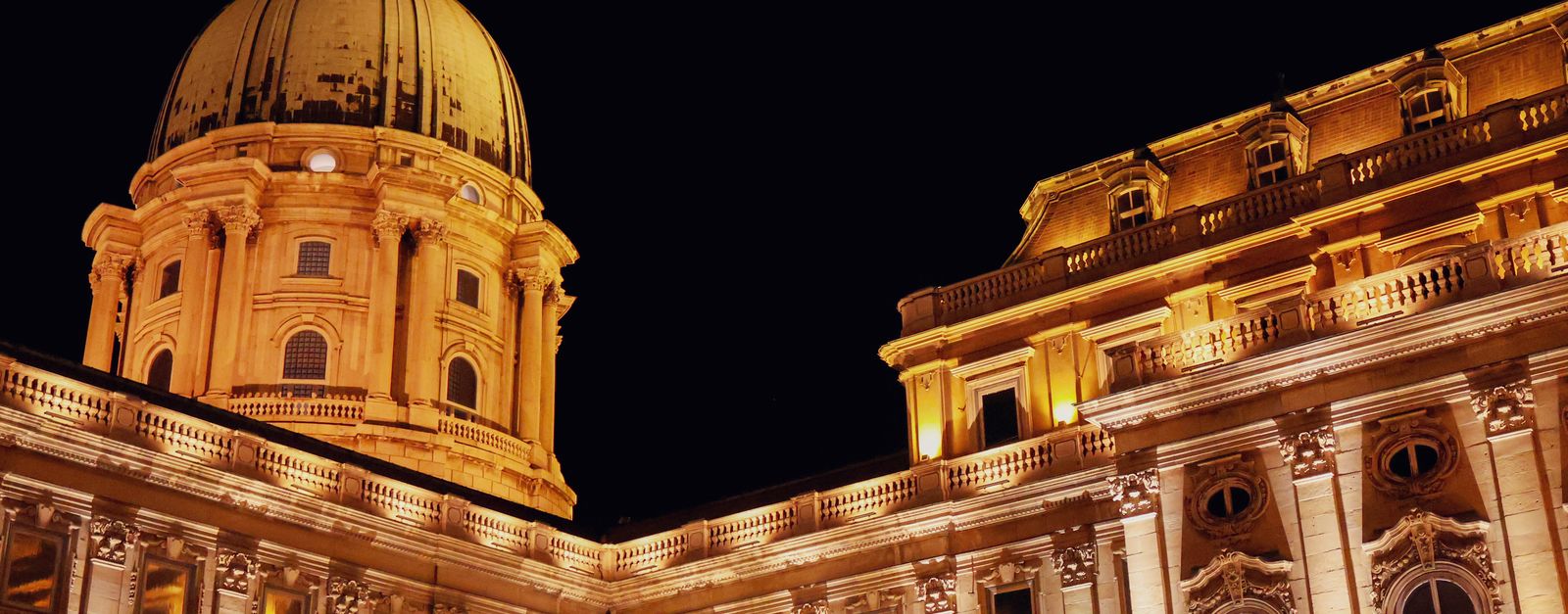 Illuminated Buda Castle dome and facade at night in Budapest, Hungary, showcasing Baroque architecture.
