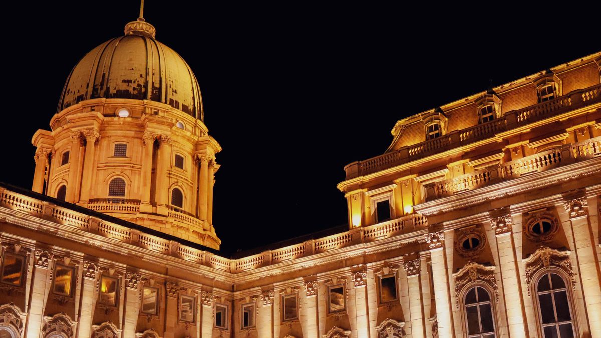 Illuminated Buda Castle dome and facade at night in Budapest, Hungary, showcasing Baroque architecture.