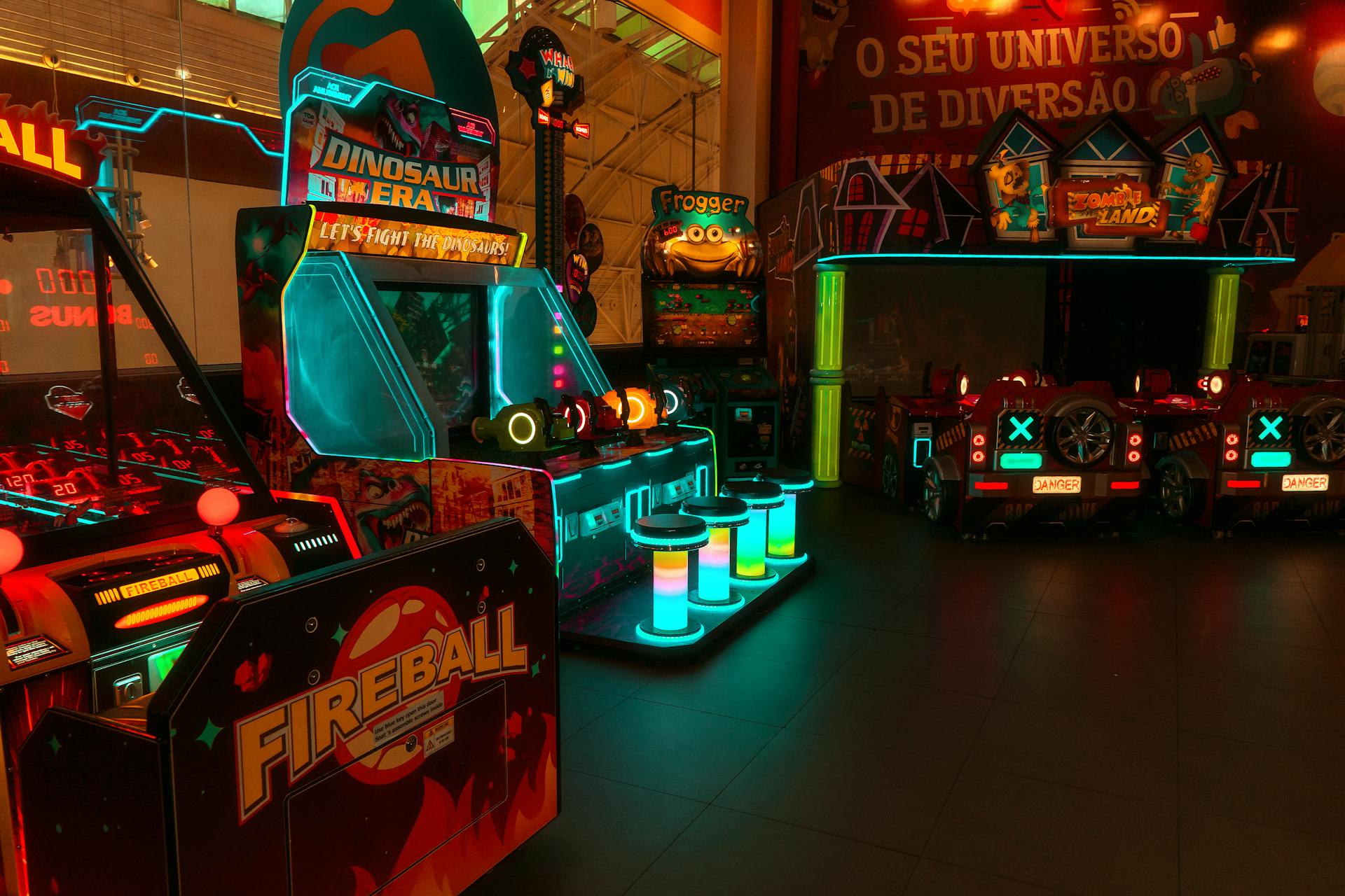 Colorful neon-lit arcade with various game machines including Fireball and Dinosaur Era.