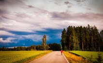 一名孤独的骑车人在阴沉天空下骑行，两旁是郁郁葱葱的田野和森林