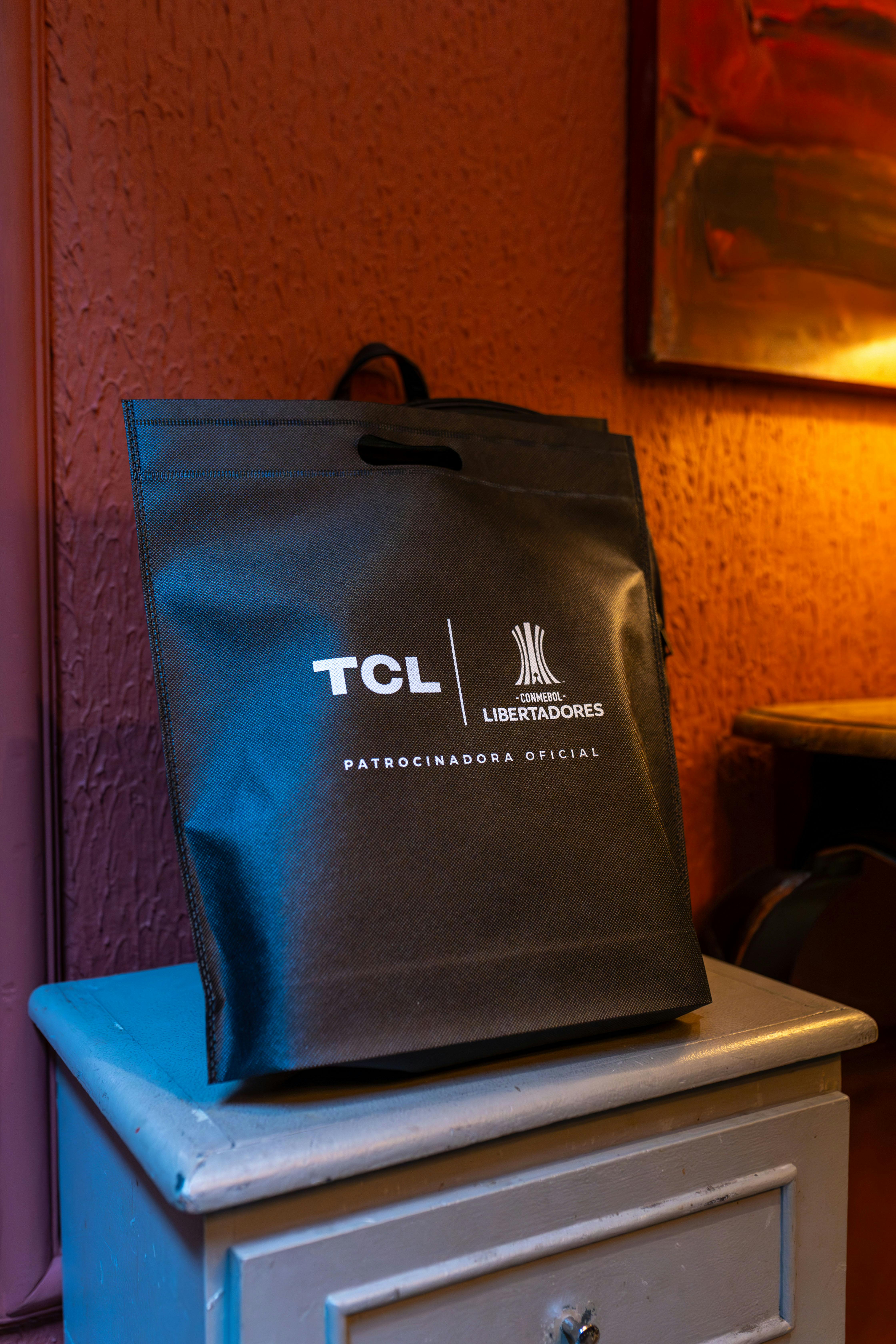 A stylish black tote bag with logos on a white side table in a warmly lit room.