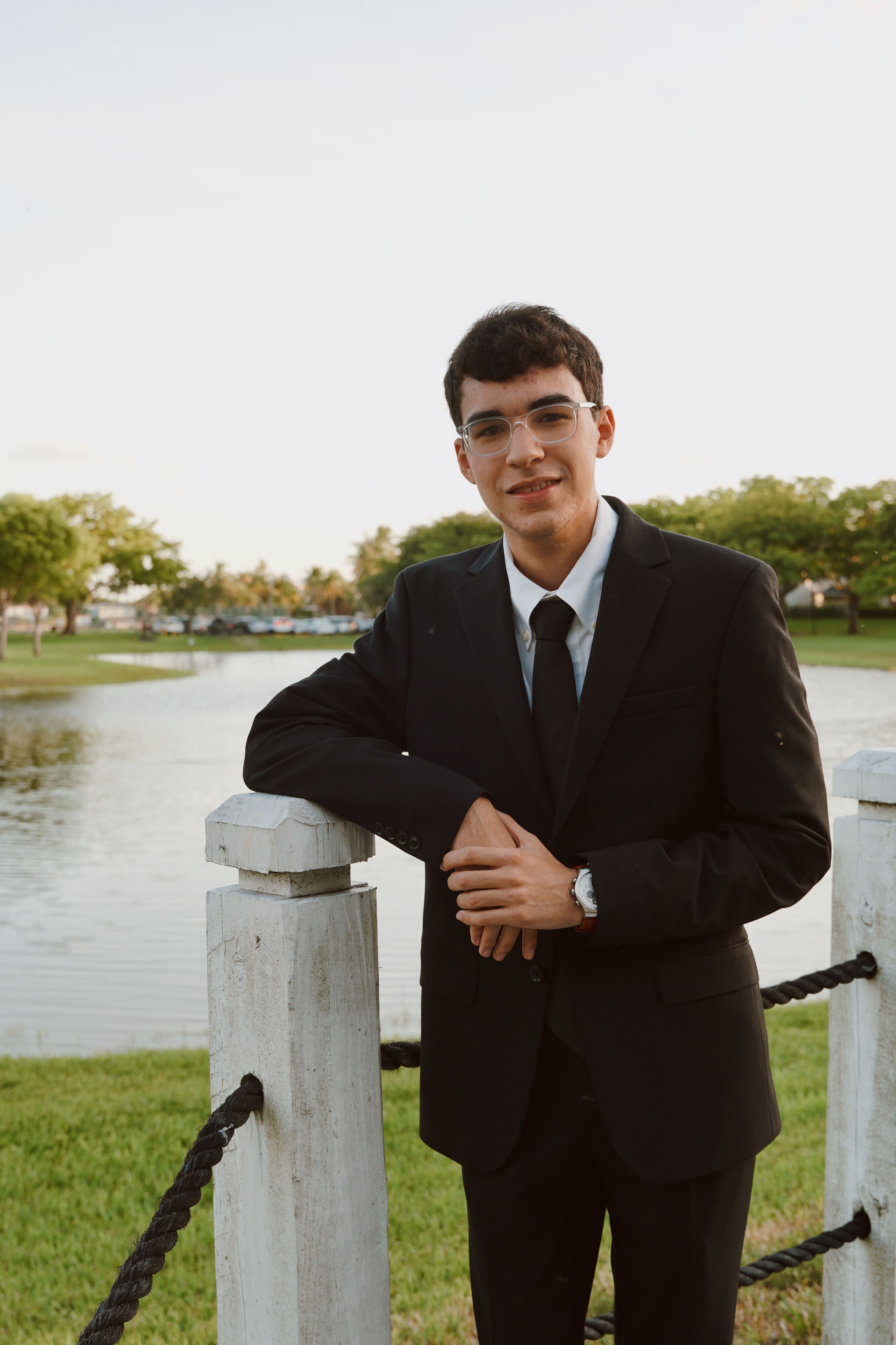 Young man in suit posing by a lake in Miami, showcasing elegant fashion.