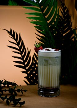 A delightful strawberry shake with foam and garnish, set amidst lush tropical leaves.