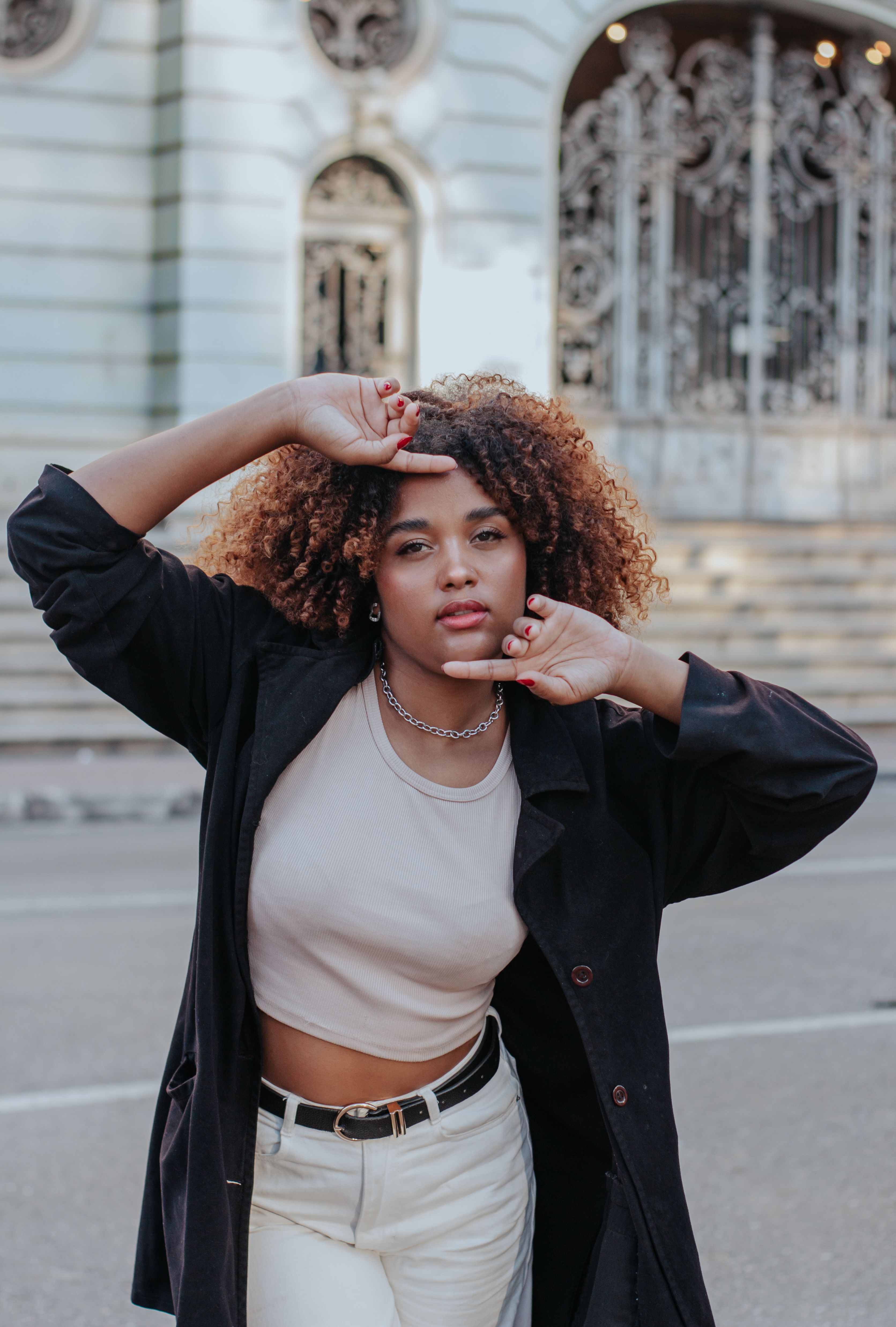 Stylish young woman with curly hair posing in city street.