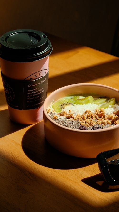 A bowl of food sits on a table next to a cup of coffee