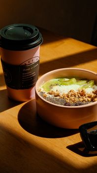 A nutritious breakfast bowl with kiwi, granola, and a coffee cup on a sunny morning.