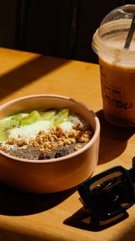 Delicious kiwi breakfast bowl with granola and iced coffee on a sunny table.