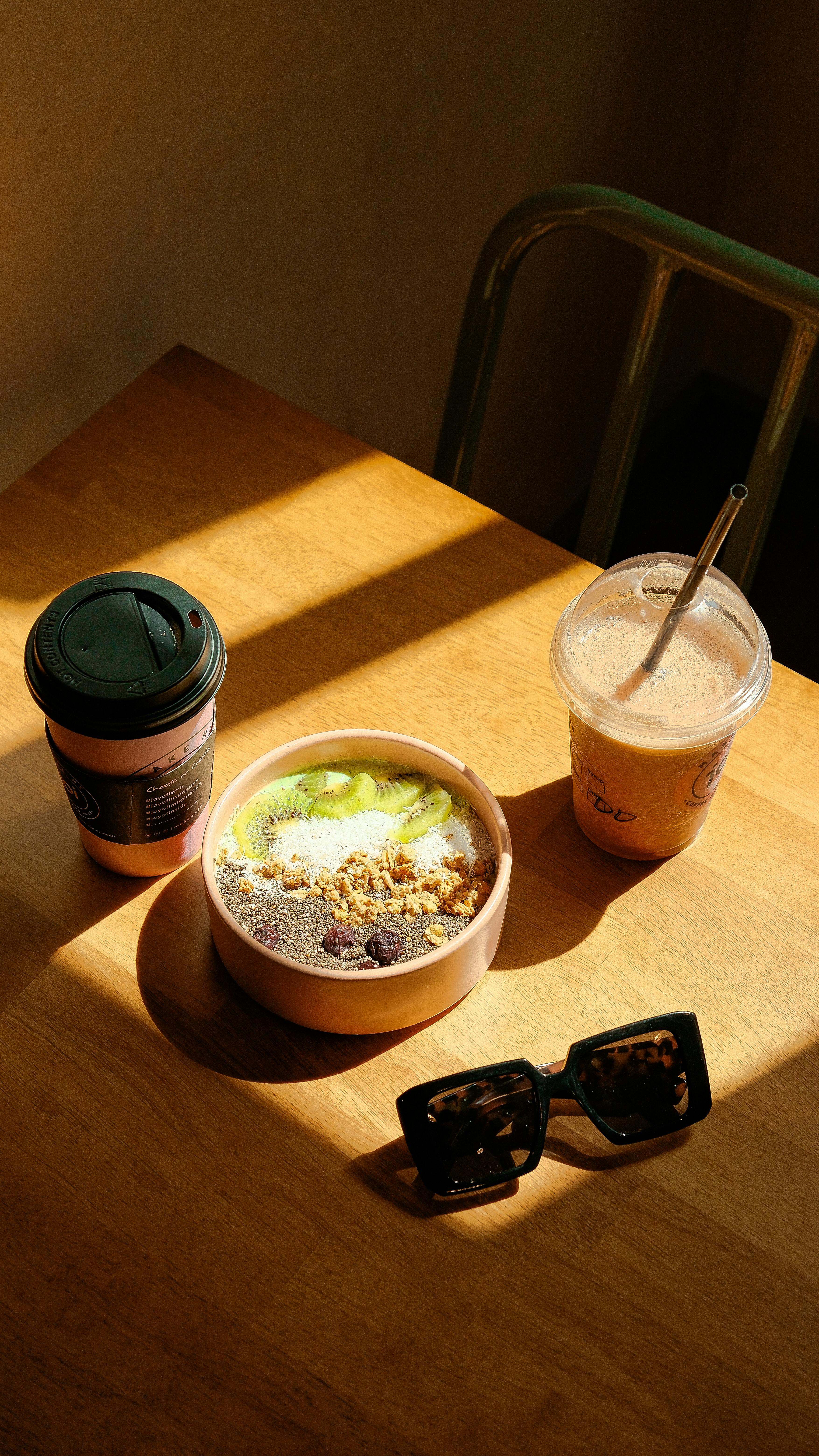 A warm morning scene with a bowl of breakfast cereal, coffee, and smoothie on a sunlit wooden table.