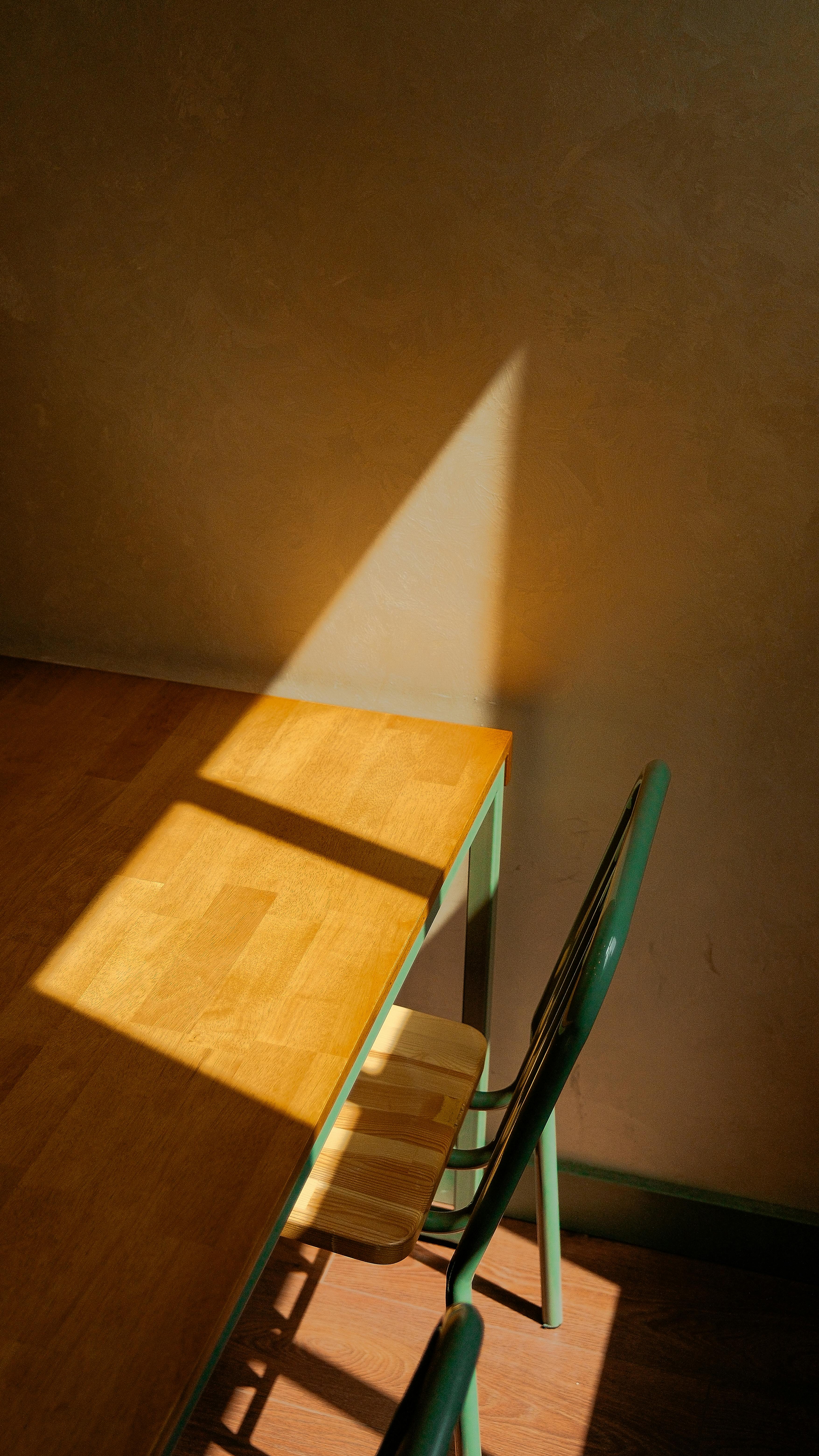Interior scene with sunlight casting shadows on a wooden table and metal chair.