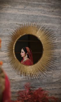 Elegant Indian bride in traditional attire reflected in a gold round mirror.