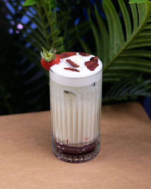 Free Delicious strawberry cocktail topped with fresh fruit surrounded by tropical leaves. Stock Photo