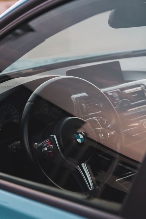 Free Close-up of a BMW car steering wheel through the car window, showcasing the vehicle's modern interior design. Stock Photo